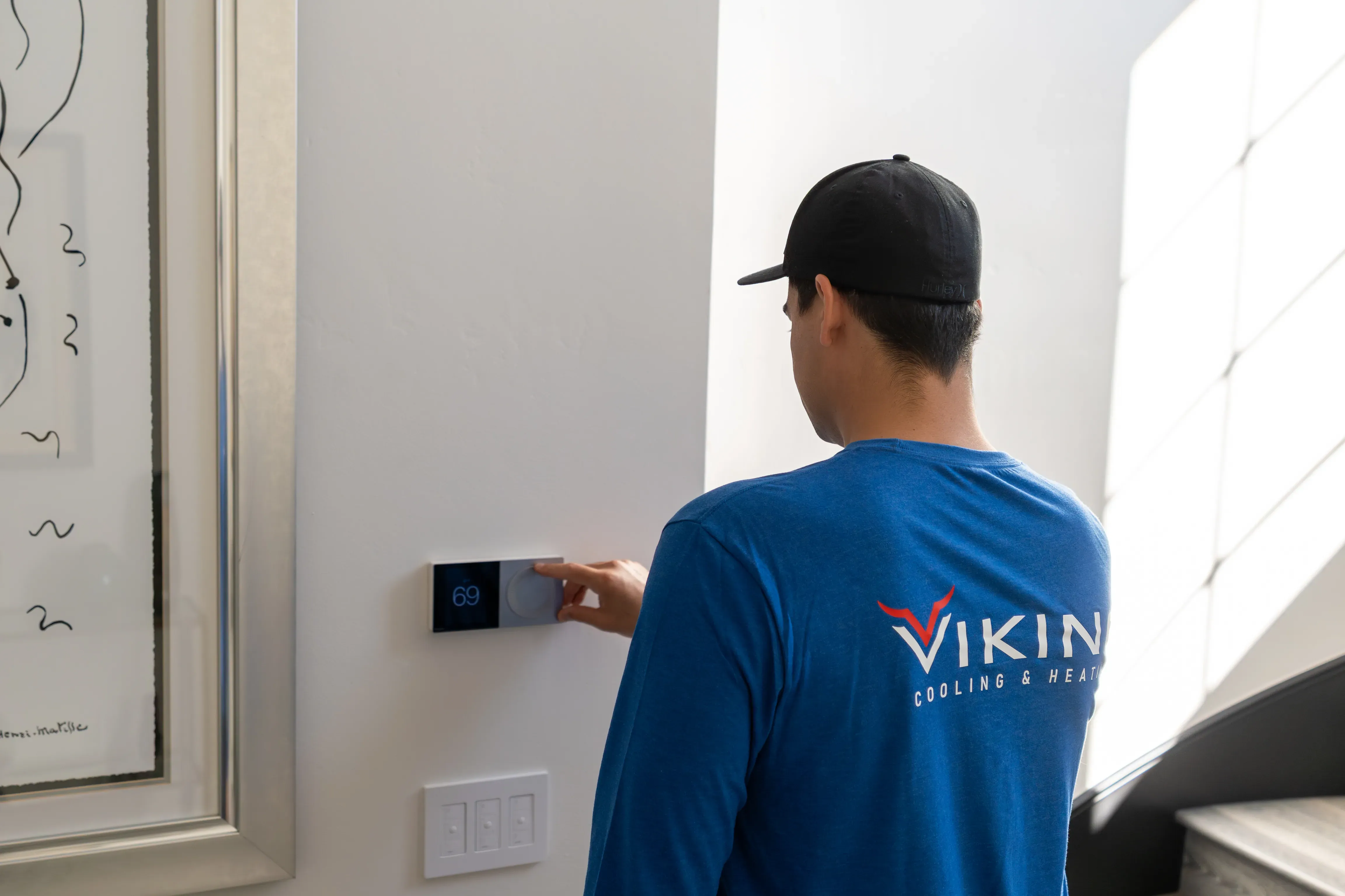 A Viking technician adjusting a smart thermostat on a homeowner’s wall